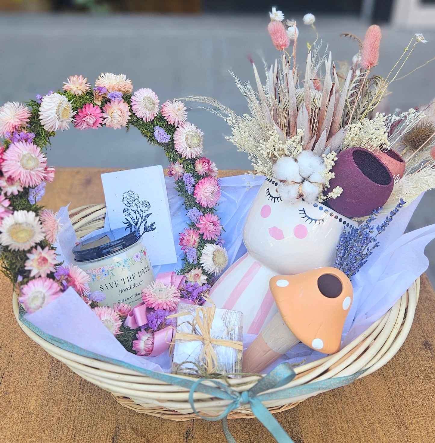 Decorative basket with flowers, a candle, and a small figurine on a wooden surface.