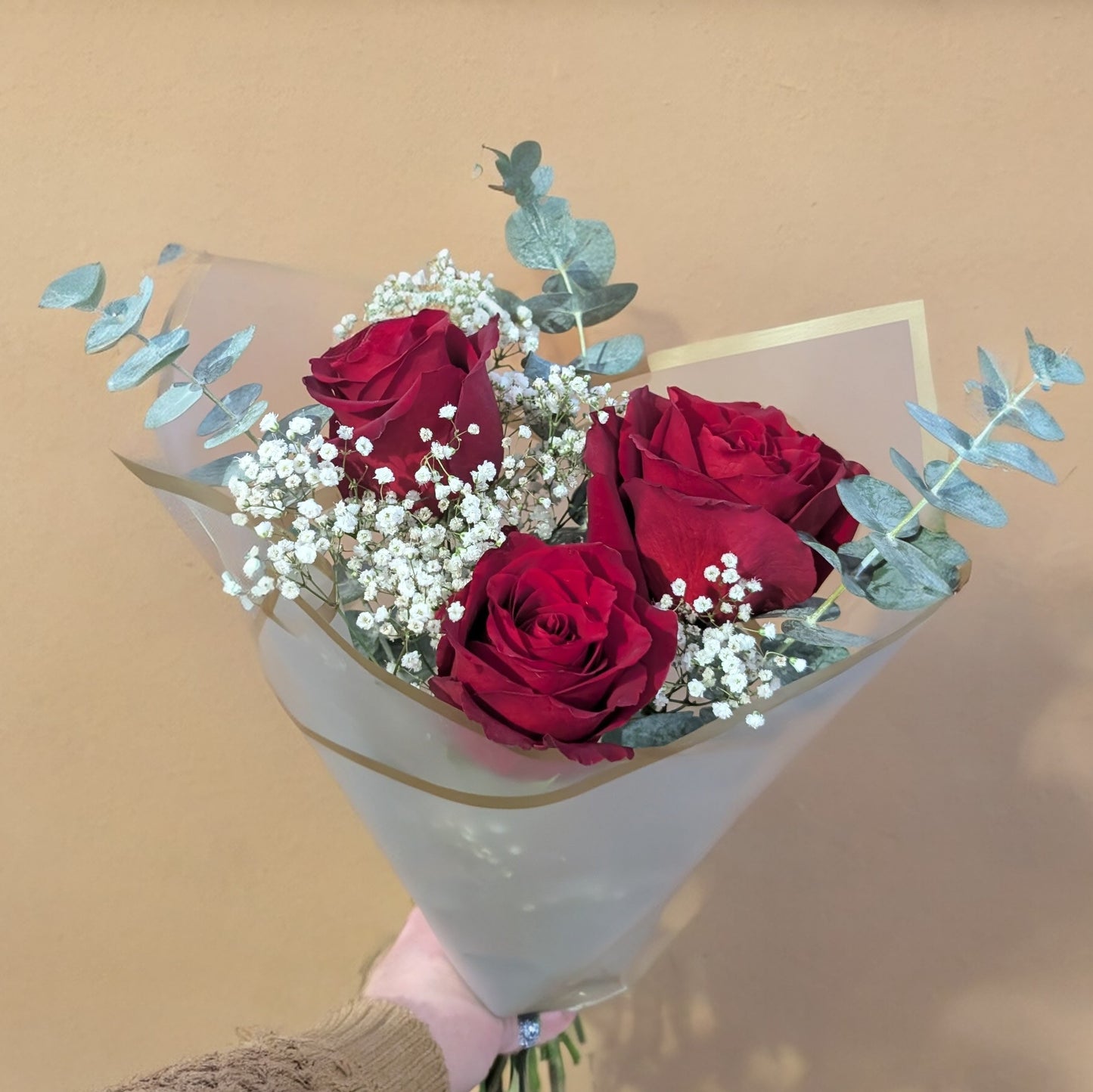 Bouquet of red roses with baby's breath held against a beige background