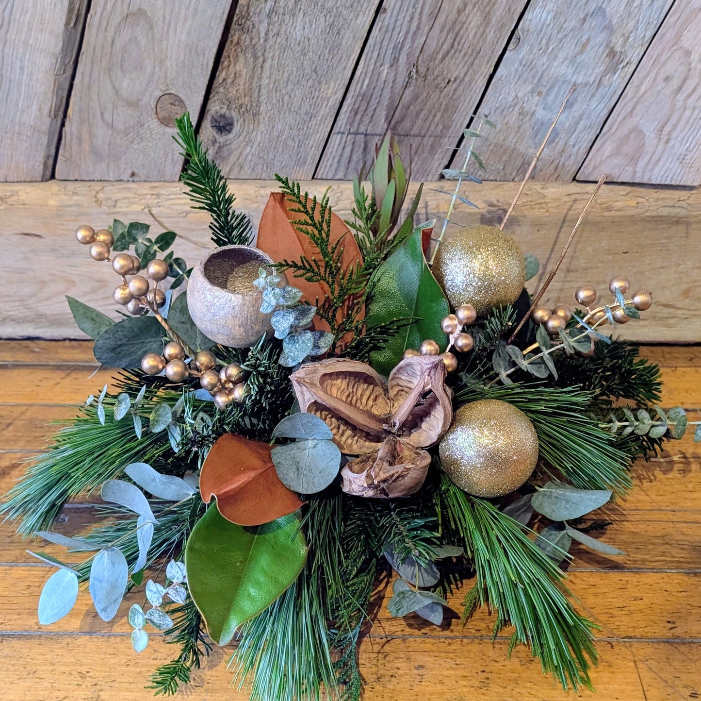 Decorative arrangement with greenery, gold ornaments, and nuts on a wooden surface