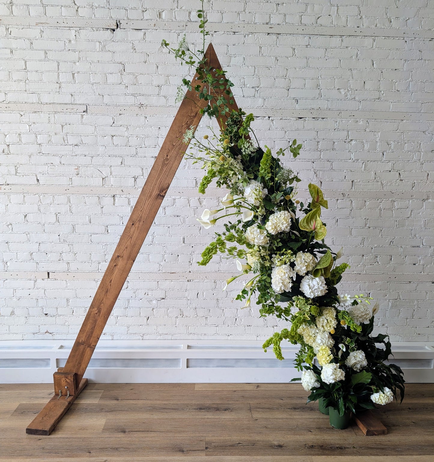 Wooden triangle frame with floral decorations against a white brick wall.