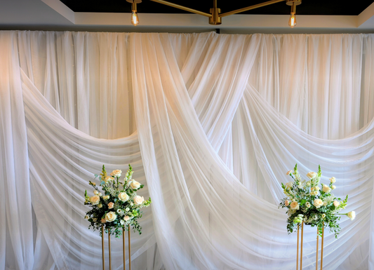 White draped fabric backdrop with floral arrangements on stands